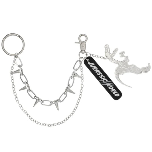 A silver metal keychain from the USJ UNIVRS collection featuring a dinosaur skeleton charm, a black tag that says 'JURASSIC WORLD', and a chain with small spikes.