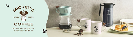 Disney Store Japan Life with Cafe collection banner. Features a mint green Mickey Mouse coffee dripper, glass server, white Mickey and Minnie mugs with biscuit-shaped handles, and a navy blue stainless steel coffee pot.