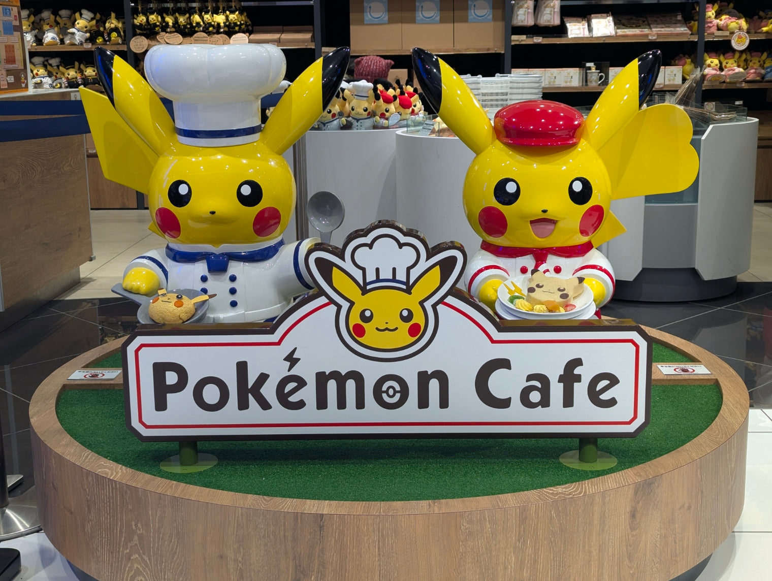 A display of exclusive merchandise from the Pokémon Cafe in Japan. The image features a "Chef Pikachu" plush toy wearing a red hat and apron, alongside a "Waitress Pikachu" plush.