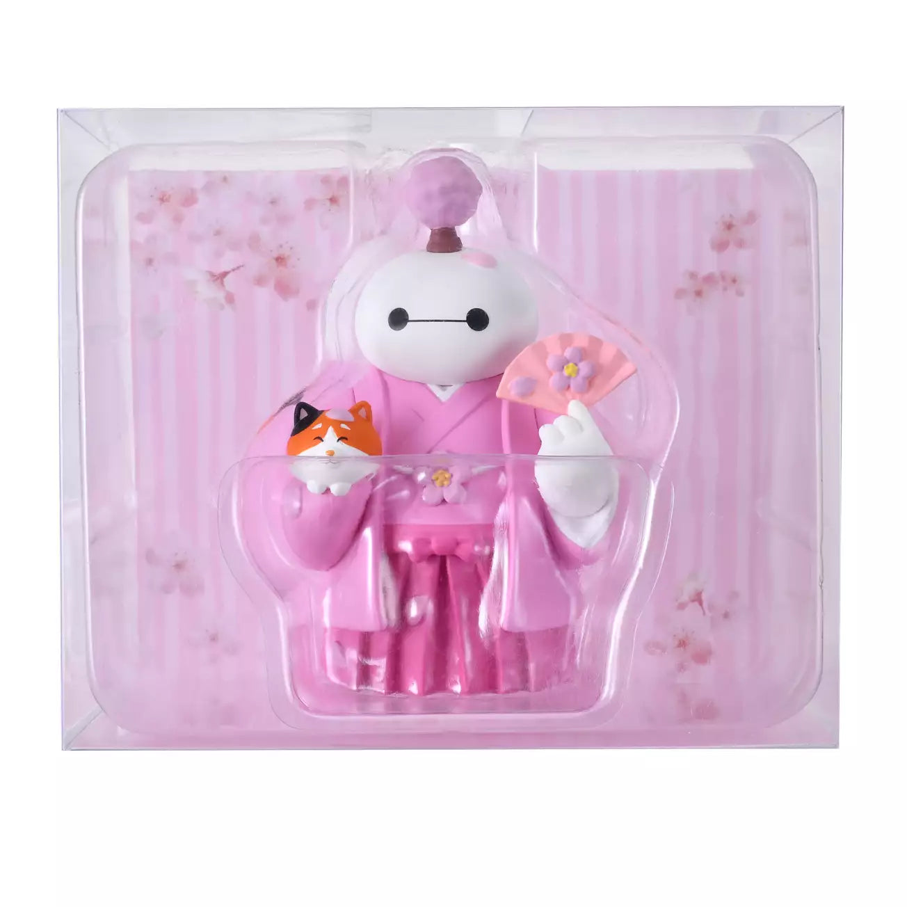 An adorable figure of Baymax from Big Hero 6 dressed in a traditional pink kimono and hakama for the cherry blossom season. Baymax holds a pink fan with a flower design in one hand and cradles Mochi the cat (also smiling) in the other arm. A small cherry blossom tree sprouts from Baymax's head. The setting is a festive pink sakura background.