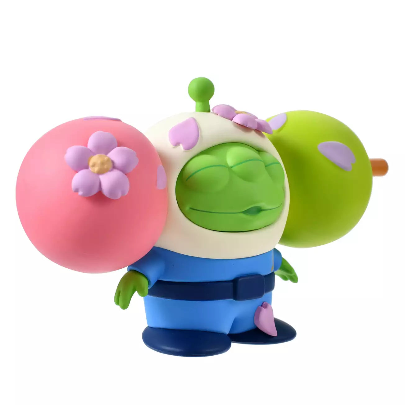 A funny and creative figure of a Little Green Man (Alien) reimagined as a 'Hanami Dango' skewer. The Alien's head is the center green dumpling, sandwiched between a pink dumpling on the left and a lime green dumpling on the right. The character wears a blue space suit body below the dango head. Pink flower petals decorate the dumplings.