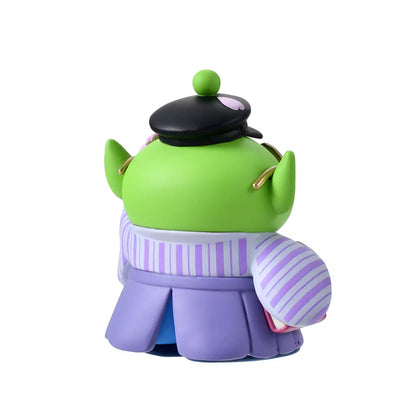 A Disney Store Japan exclusive figure of a Little Green Man (Alien) from Toy Story. The character is dressed in a traditional Japanese purple striped hakama and wears a black student cap. It poses with a book in one hand and touches its glasses with the other. The figure is set against a pink striped background with falling cherry blossom petals.