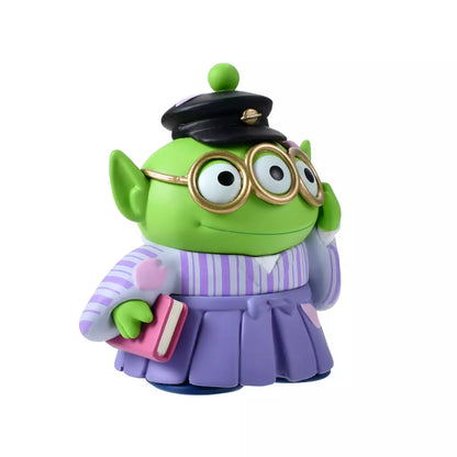 A Disney Store Japan exclusive figure of a Little Green Man (Alien) from Toy Story. The character is dressed in a traditional Japanese purple striped hakama and wears a black student cap. It poses with a book in one hand and touches its glasses with the other. The figure is set against a pink striped background with falling cherry blossom petals.