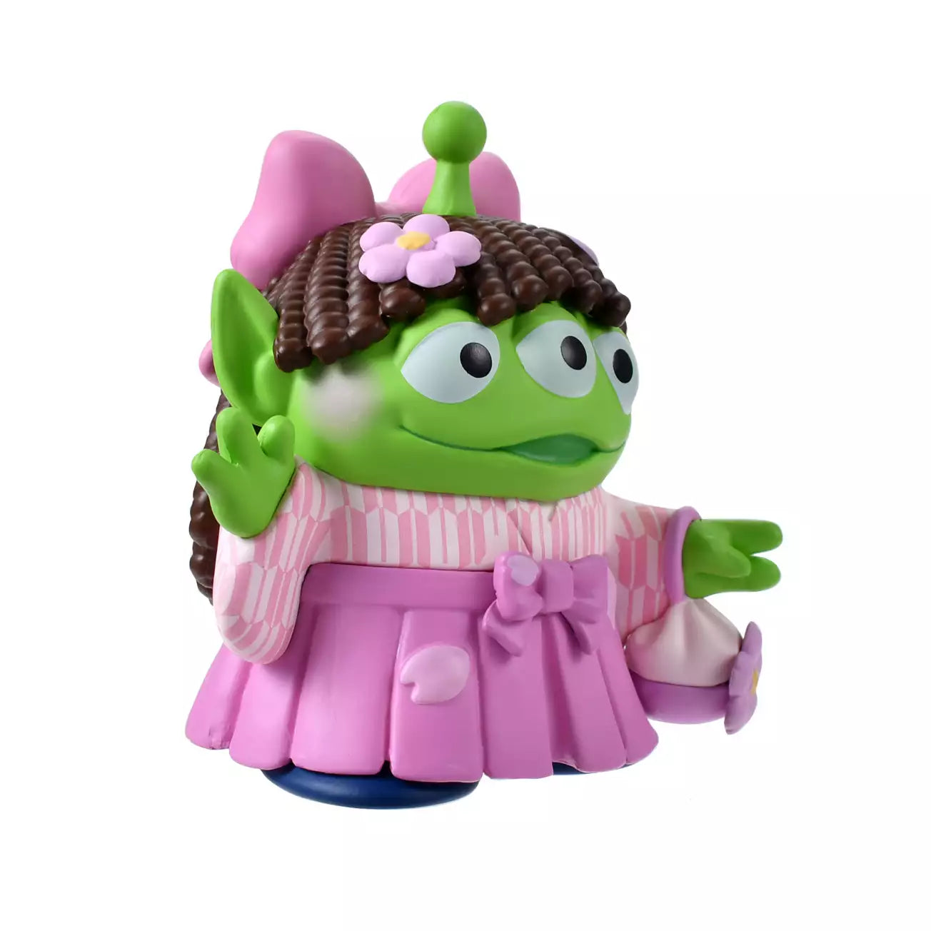 A cute collectible figure of a Little Green Man (Alien) wearing a pink wig with brown pigtails and a traditional pink hakama kimono. The character holds a small flower-shaped purse and waves with one hand. The backdrop features a pink striped pattern with delicate cherry blossom illustrations.