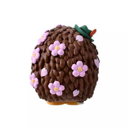 A figure of Mr. Pricklepants from Toy Story 3 enjoying a spring picnic. The hedgehog wears green lederhosen and a small green hat. He holds a 'Hanami Dango' (a three-colored sweet dumpling) in one hand and has a crown of pink cherry blossoms on his head. The background is pink with falling sakura petals.