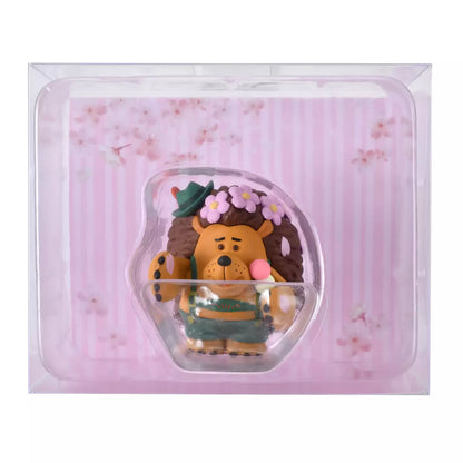 A figure of Mr. Pricklepants from Toy Story 3 enjoying a spring picnic. The hedgehog wears green lederhosen and a small green hat. He holds a 'Hanami Dango' (a three-colored sweet dumpling) in one hand and has a crown of pink cherry blossoms on his head. The background is pink with falling sakura petals.