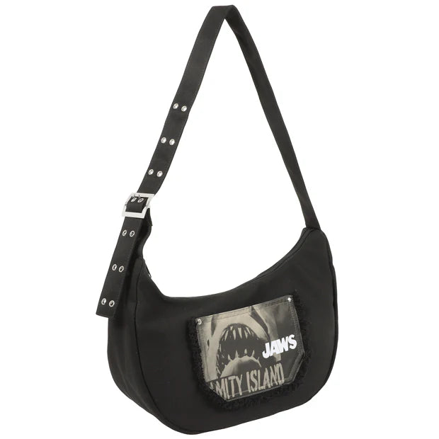 A black shoulder bag from the USJ UNIVRS collection featuring a pocket with a graphic of the shark from Jaws and the text 'JAWS' and 'AMITY ISLAND'.