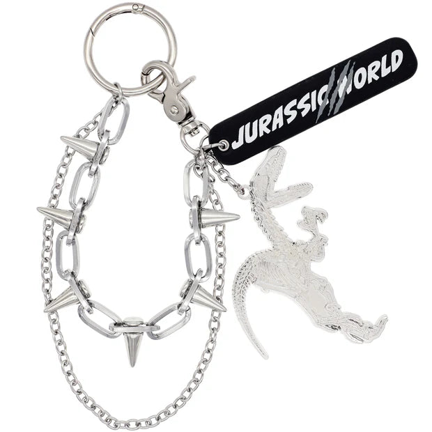 A silver metal keychain from the USJ UNIVRS collection featuring a dinosaur skeleton charm, a black tag that says 'JURASSIC WORLD', and a chain with small spikes.
