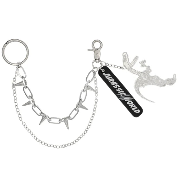 A silver metal keychain from the USJ UNIVRS collection featuring a dinosaur skeleton charm, a black tag that says 'JURASSIC WORLD', and a chain with small spikes.
