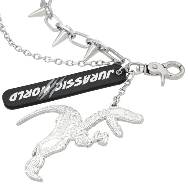 A silver metal keychain from the USJ UNIVRS collection featuring a dinosaur skeleton charm, a black tag that says 'JURASSIC WORLD', and a chain with small spikes.
