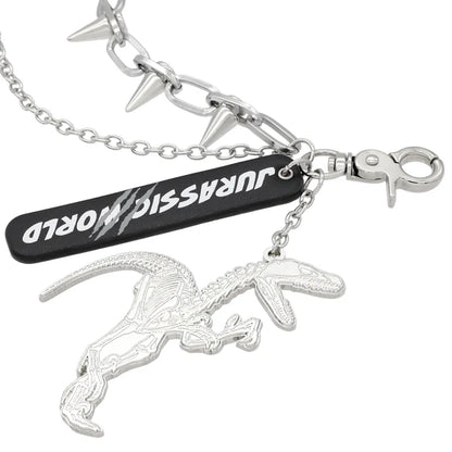 A silver metal keychain from the USJ UNIVRS collection featuring a dinosaur skeleton charm, a black tag that says 'JURASSIC WORLD', and a chain with small spikes.