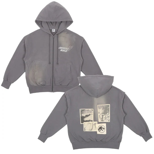 A grey zip-up hoodie from the USJ UNIVRS collection with a subtle graphic of a dinosaur scratching its claws and the text 'JURASSIC WORLD' on the front. The back features four vintage comic panels of dinosaurs.