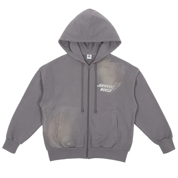 A grey zip-up hoodie from the USJ UNIVRS collection with a subtle graphic of a dinosaur scratching its claws and the text 'JURASSIC WORLD' on the front. The back features four vintage comic panels of dinosaurs.