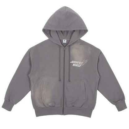 A grey zip-up hoodie from the USJ UNIVRS collection with a subtle graphic of a dinosaur scratching its claws and the text 'JURASSIC WORLD' on the front. The back features four vintage comic panels of dinosaurs.